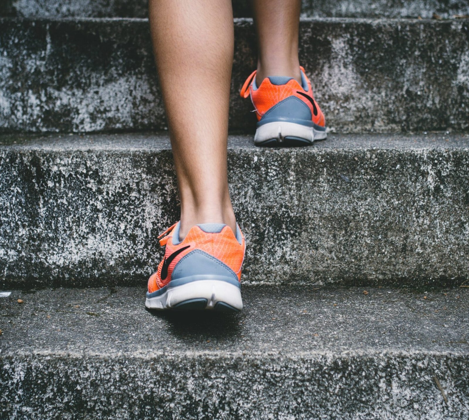 person wearing orange and gray Nike shoes walking on gray concrete stairs